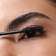 A close-up image of a person applying Nanolash mascara to their upper eyelashes using a wand.