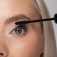 A woman uses a mascara brush to apply mascara