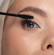 A woman carefully applies mascara to her eyelashes using a mascara brush