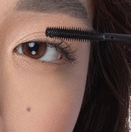 A woman is applying mascara with a brush